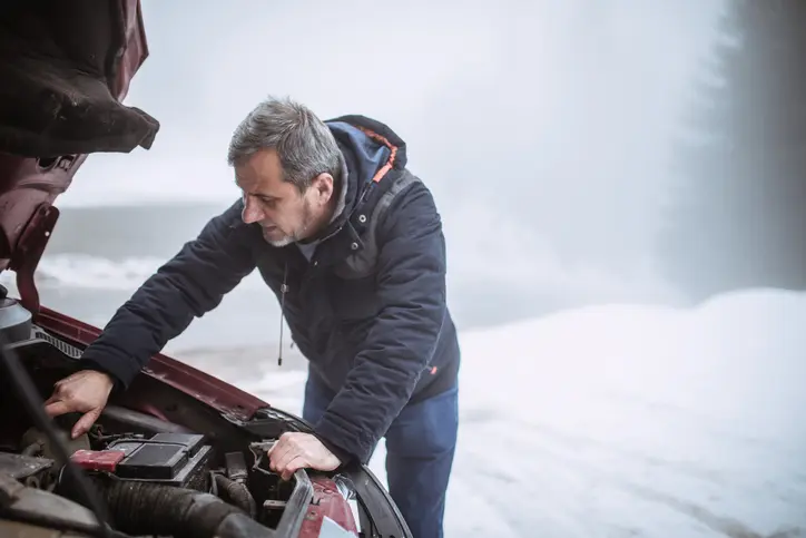 Man on the side of a snowy road with battery problems