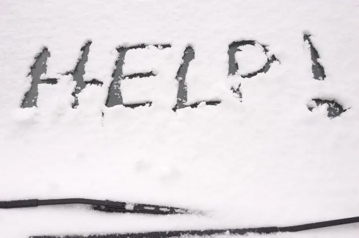 Car Windshield covered with snow and the word help written on it. A Winter Driving safety kit would have had a scraper and brush.