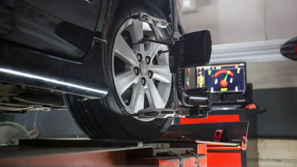 Car on lift with sensors on wheels for wheel alignment camber check in mechanic shop