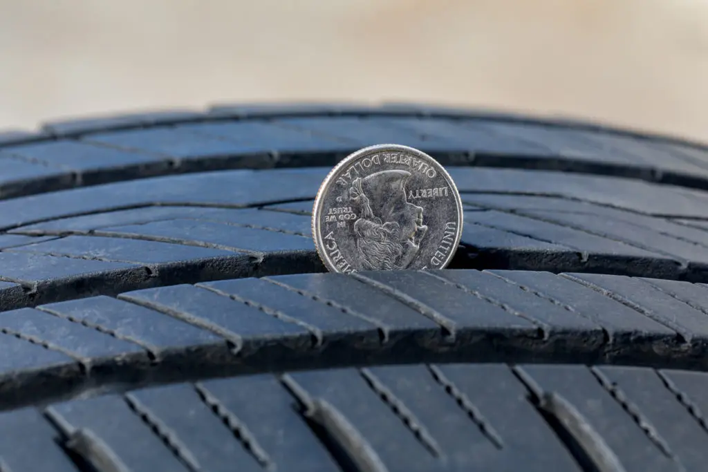 Closeup of checking tire tread wear depth of old tire using a quarter coin.