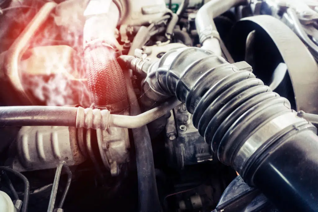 Image of a car engine overheating, as shown with the hood open and close focus on the hoses.