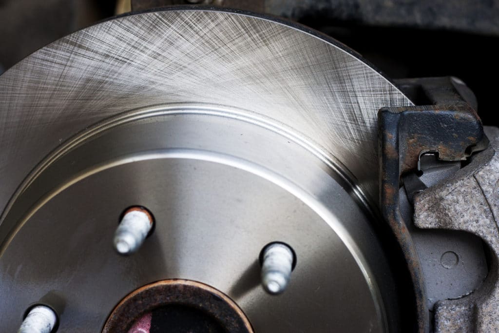 A shiny new combination disk/drum brake rotor being installed on a rear axle, with a jack and jack-stand in the background.