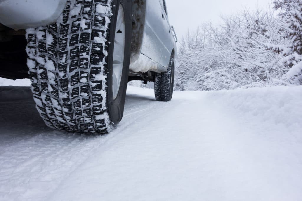 Close up of car tires driving on wintry road covered with snow