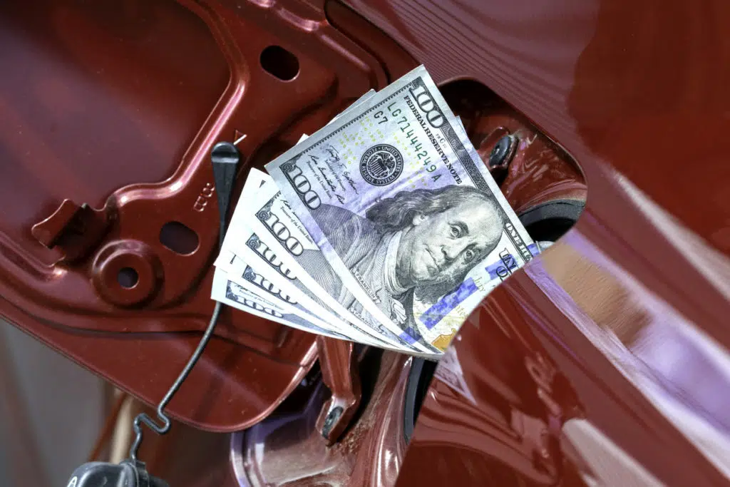 High gas prices concept image of large denomination bills stuffed into vehicle fuel tank
