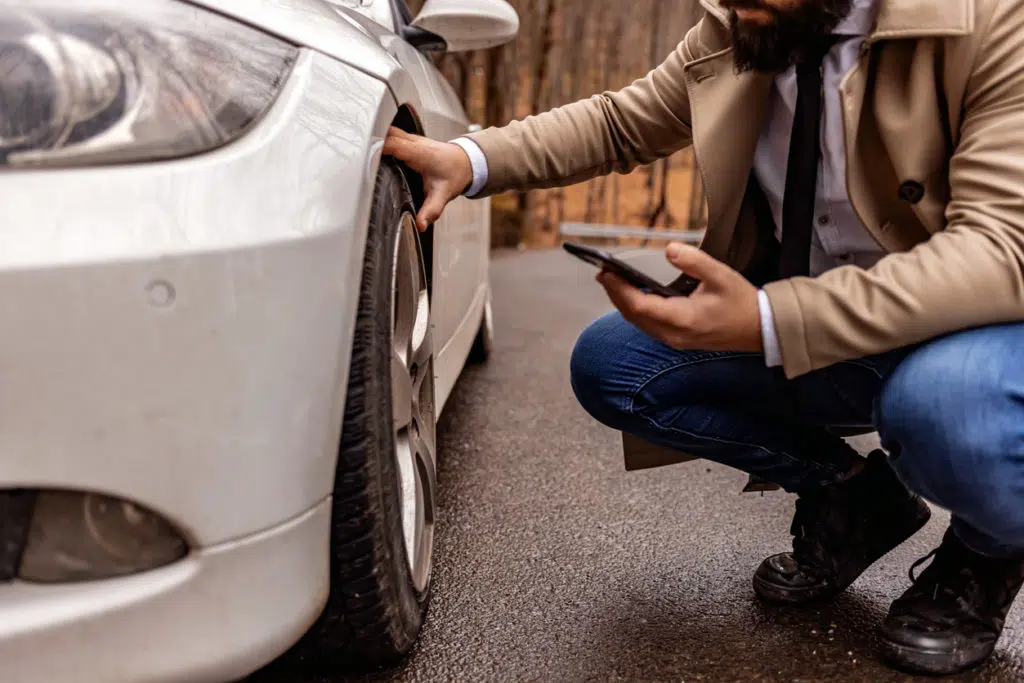 Image of a young man crouching down to inspect the front driver side tire on his car