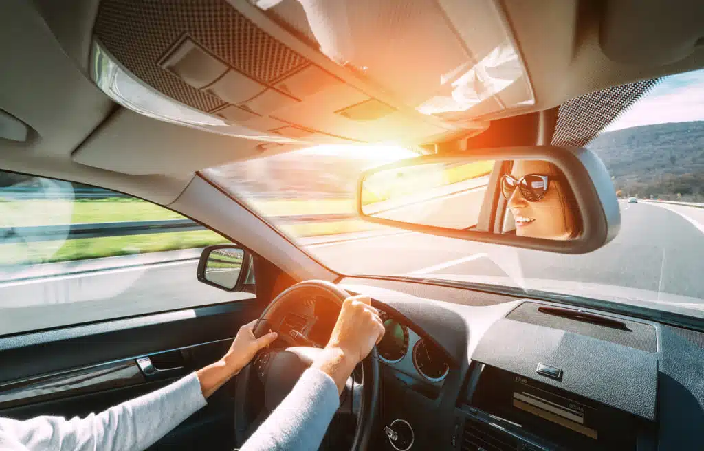 smiling woman wearing sunglasses driving car safely on open sunny highway