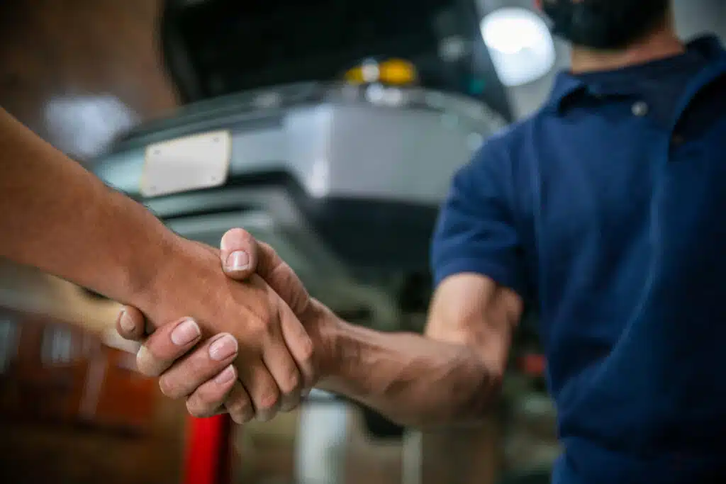 customer and mechanic at an auto repair shop shaking hands after car is repaired successfully