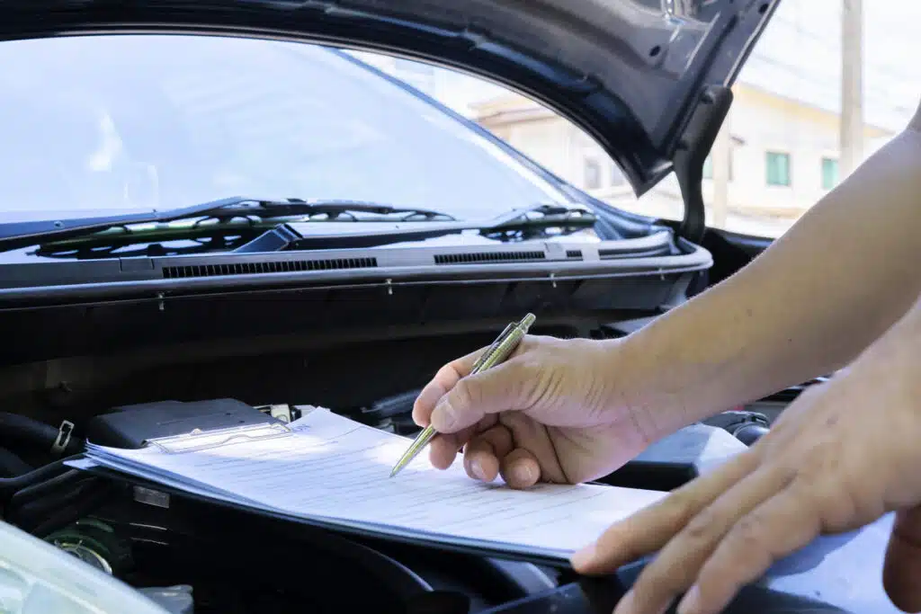 Professional auto mechanic working in repairing service, close-up. Mechaninc performing car diagnostics with a checklist.