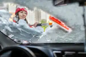Woman in winter jacket scraping ice and snow from car windows