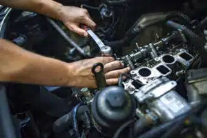 Car mechanic man at the garage fixing the engine. Hands of car mechanic with wrench in garage. Close up hands of unrecognizable mechanic doing car service and maintenance. Auto Service Business Concept. Pro Car Mechanic Taking Care of Vehicle. Checking Under the Car Hood.