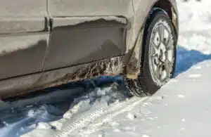 dirty car driving in winter snow. closeup on tire and undercarriage showing salt, ice, and road grime