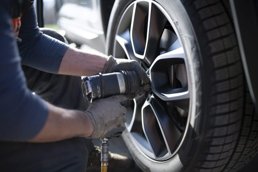 Close-up shot of an unrecognizable auto repairman changing whleel and tire in a workshop.